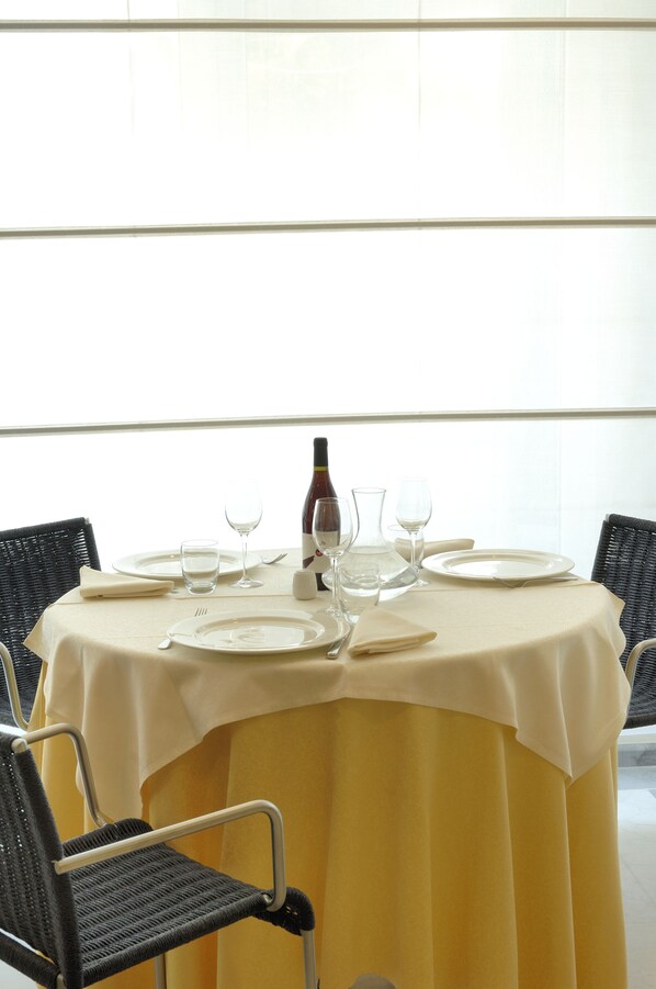 Mesa de comedor preparada para cuatro personas, con mantel amarillo, cuatro sillas, copas de vino y una botella.