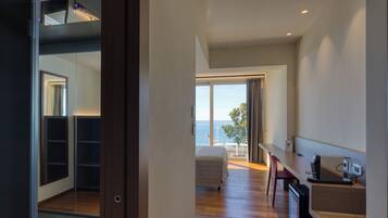 Une chambre d’hôtel moderne avec balcon, un lit, un bureau avec un ordinateur et une vue sur la mer.