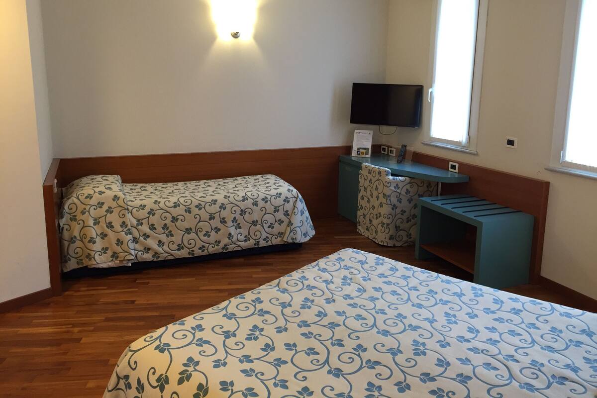 A hotel room with a wooden bed, a desk with a chair, a television, and a window with blinds.
