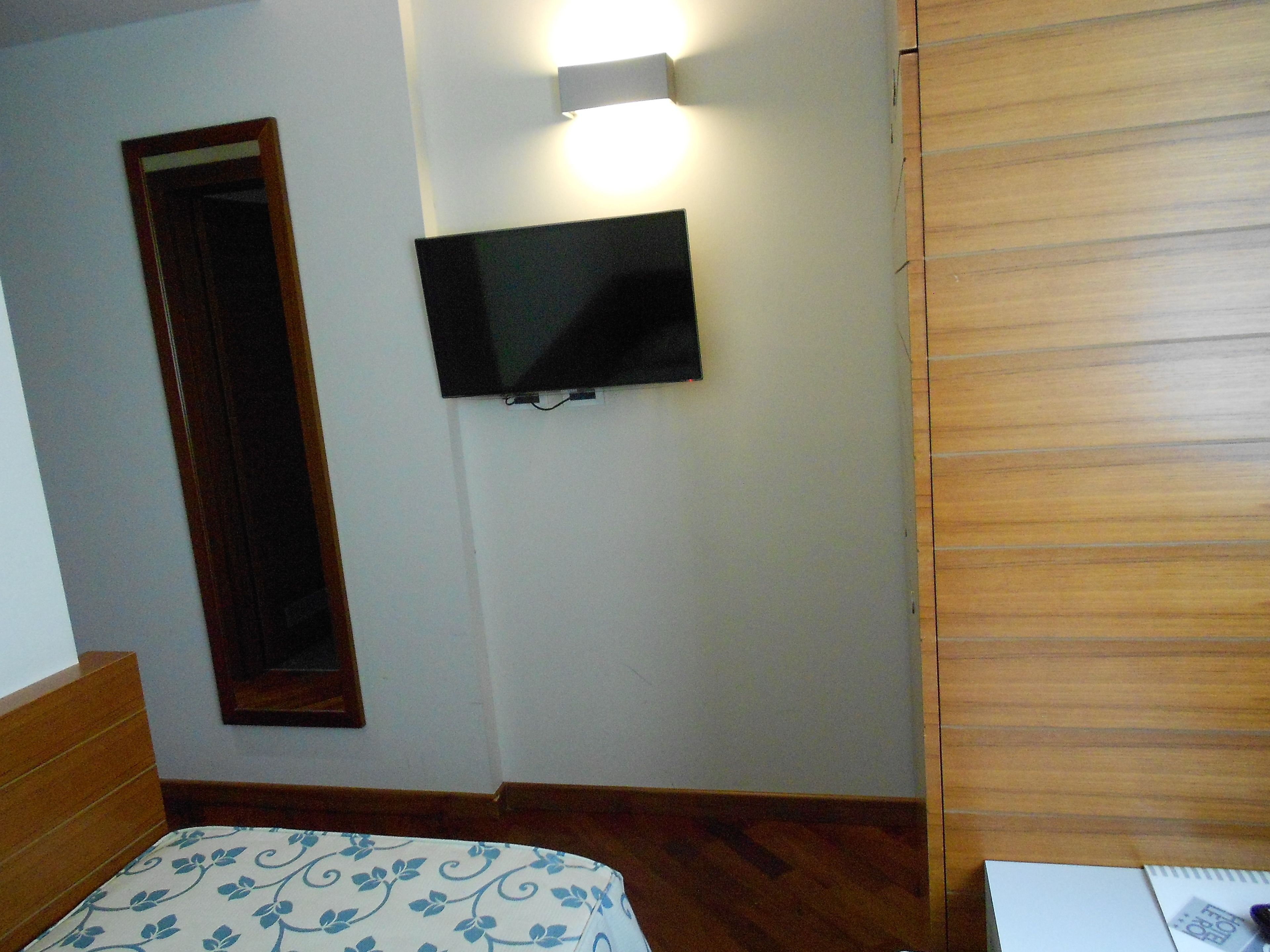 A bedroom with a bed, a TV mounted on the wall, and a wooden door.