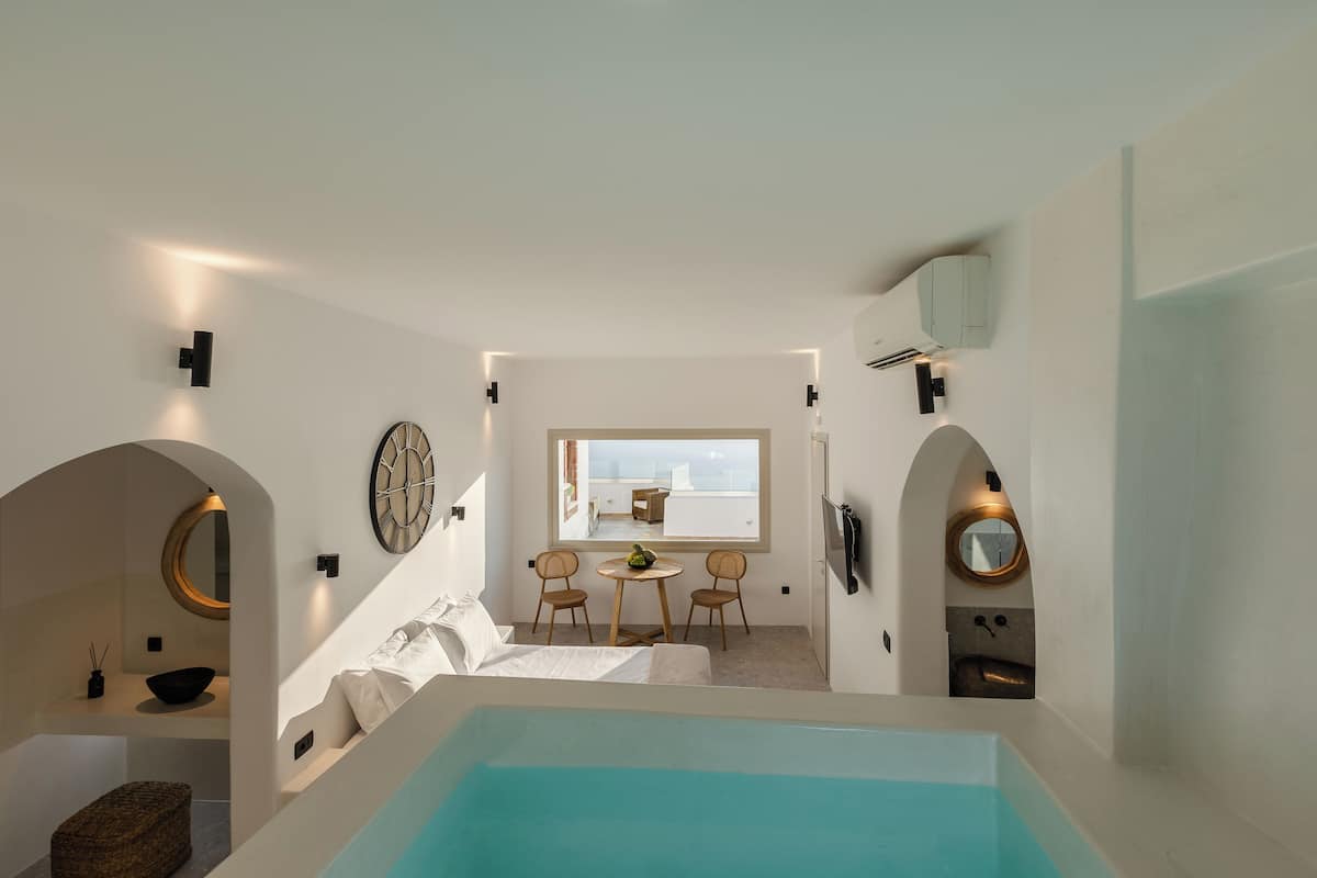 Habitación de hotel moderna con una bañera grande, un área de comedor con dos sillas, un espejo redondo y vistas a la ciudad.