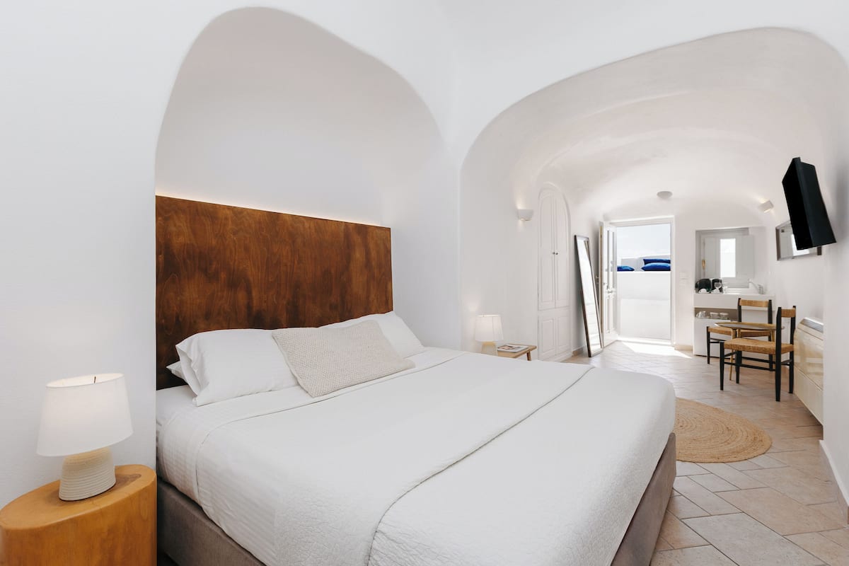Un dormitorio moderno con una cama grande, cabecera de madera, lámparas de noche, un televisor de pantalla plana y vistas al mar a través de una puerta abierta.