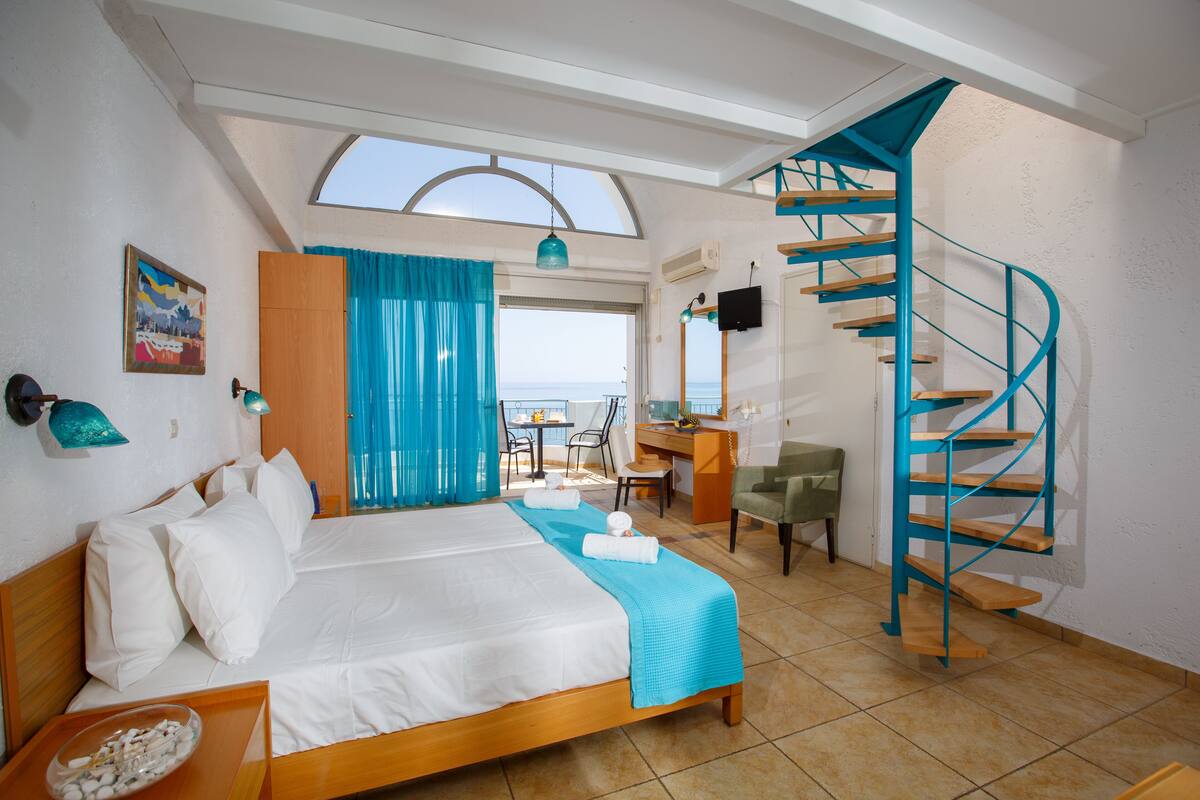 Ein Schlafzimmer mit Bett, Schreibtisch, Stuhl und einer Wendeltreppe, mit Blick aufs Meer.