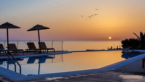 Un espace aménagé au bord de la piscine, avec des chaises longues et des parasols, offrant une vue sur une étendue d’eau calme au coucher du soleil.