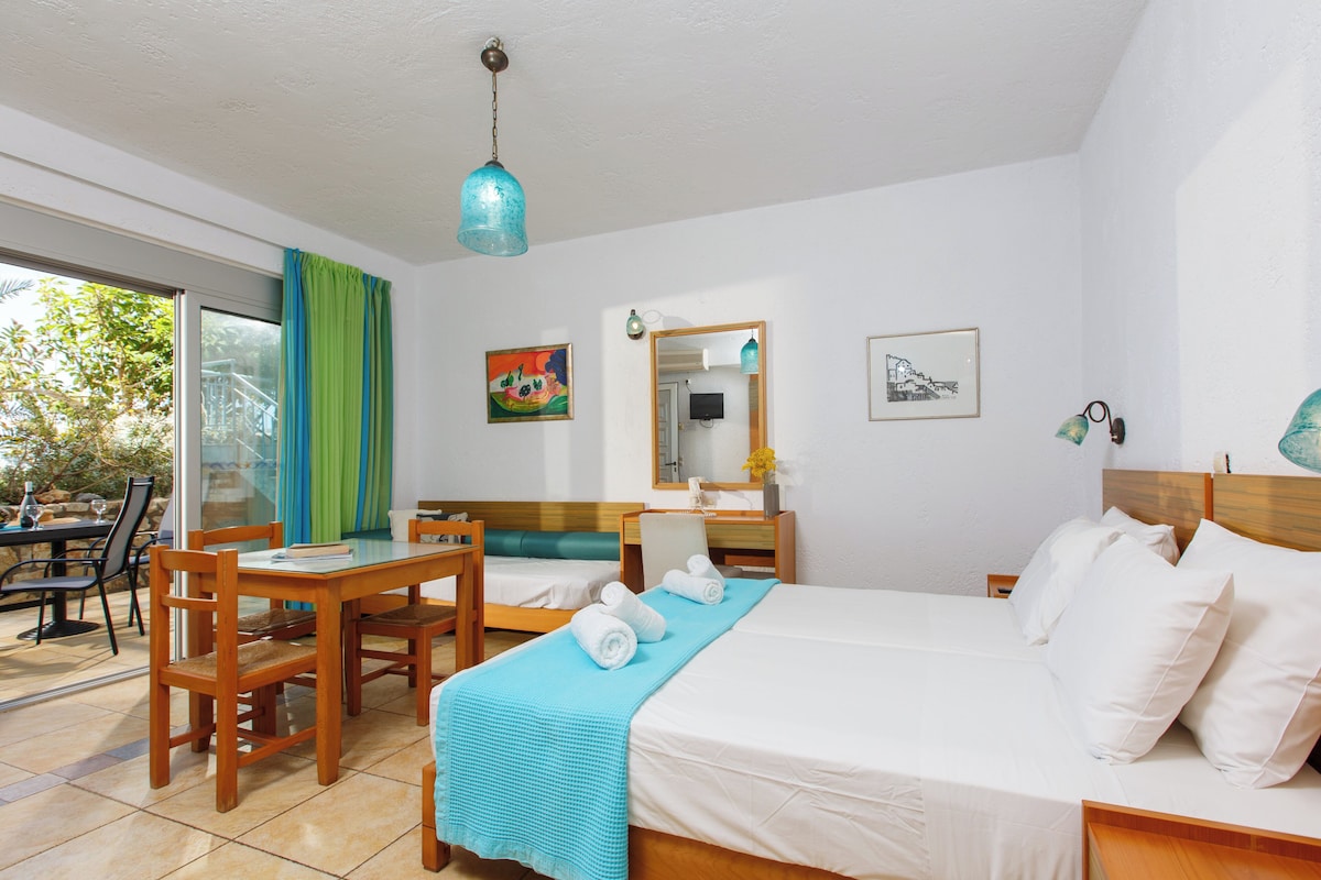 Une chambre d’hôtel avec un lit, un bureau et une chaise. Il y a une fenêtre avec des rideaux, un miroir et des œuvres d’art accrochées aux murs.