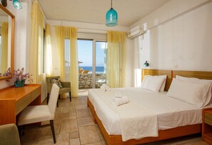 Ein Hotelzimmer mit Bett, Schreibtisch, Stuhl, einem Fenster mit Vorhängen und Meerblick.