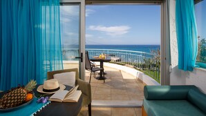 A balcony with a view of the ocean, a table with a hat and book, and a green sofa. - Romantica Beach Villas (Hersonissos)