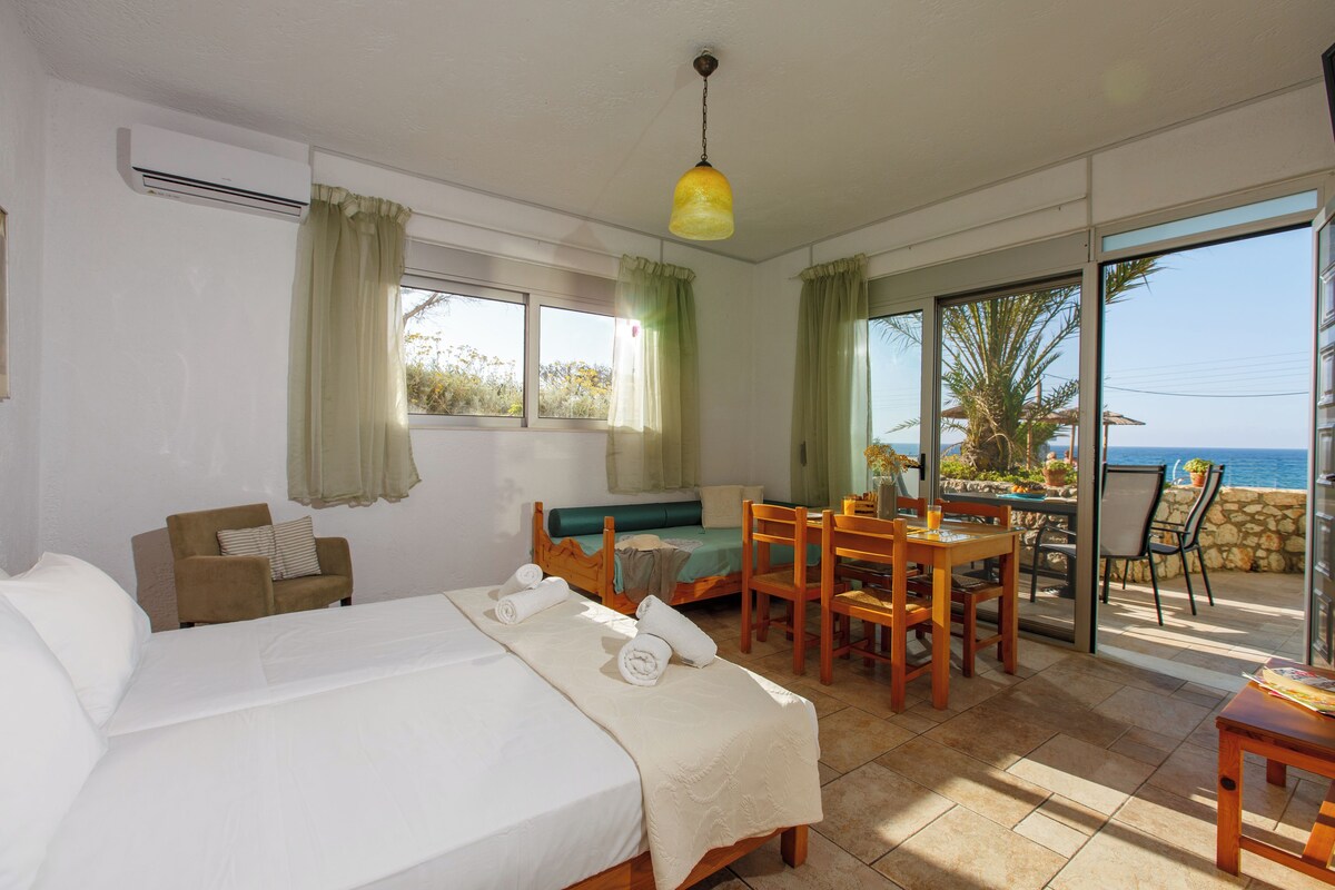 Een slaapkamer met een bed, een bank, een eettafel met stoelen, en een balkon met uitzicht op zee.