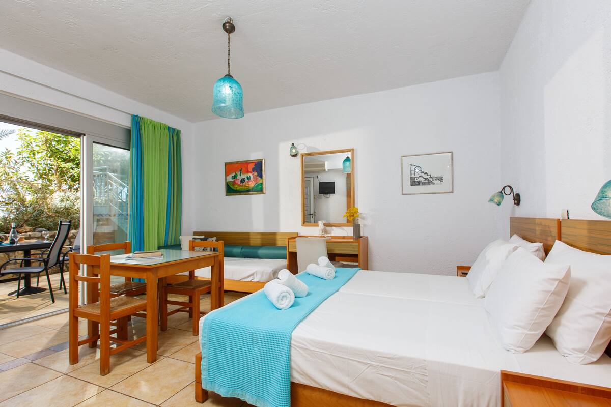 Ein Hotelzimmer mit einem Bett, einem Schreibtisch und einem Sessel. Ein Fenster mit Vorhängen, ein Spiegel und Kunstwerke schmücken die Wände.