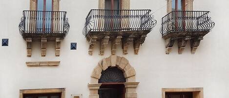 A building with three balconies, a central archway, and two doors.