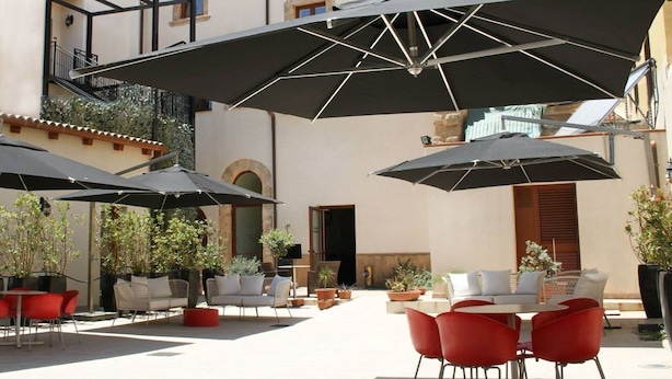 An outdoor patio area with multiple tables and chairs, some under large umbrellas, and potted plants around. - Hotel Palazzo Zuppello (Augusta)