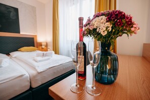 Une chambre d’hôtel avec un lit, une table de chevet en bois, un vase de fleurs et une bouteille de vin.