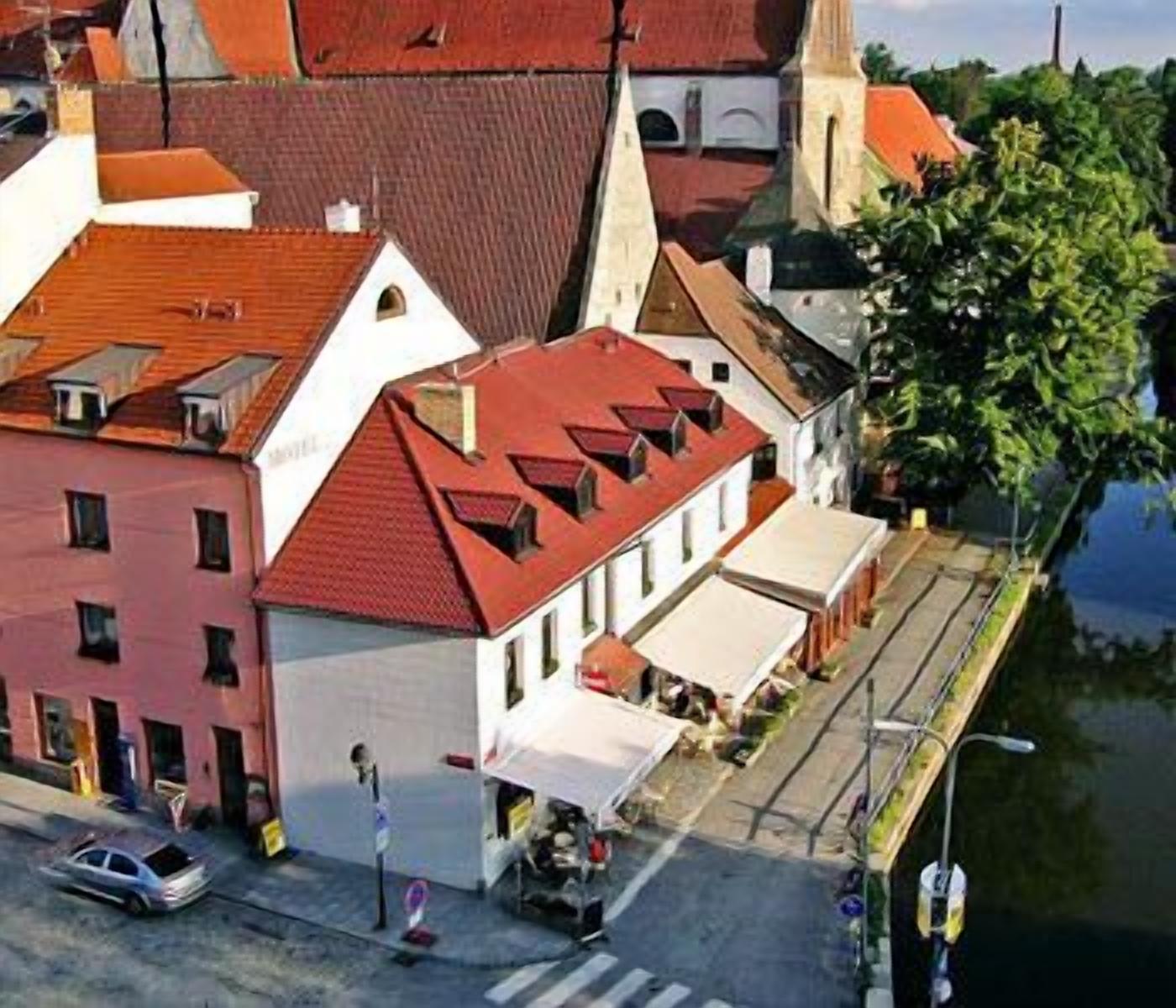 A street view with a building featuring a red roof and a church with a tall spire.