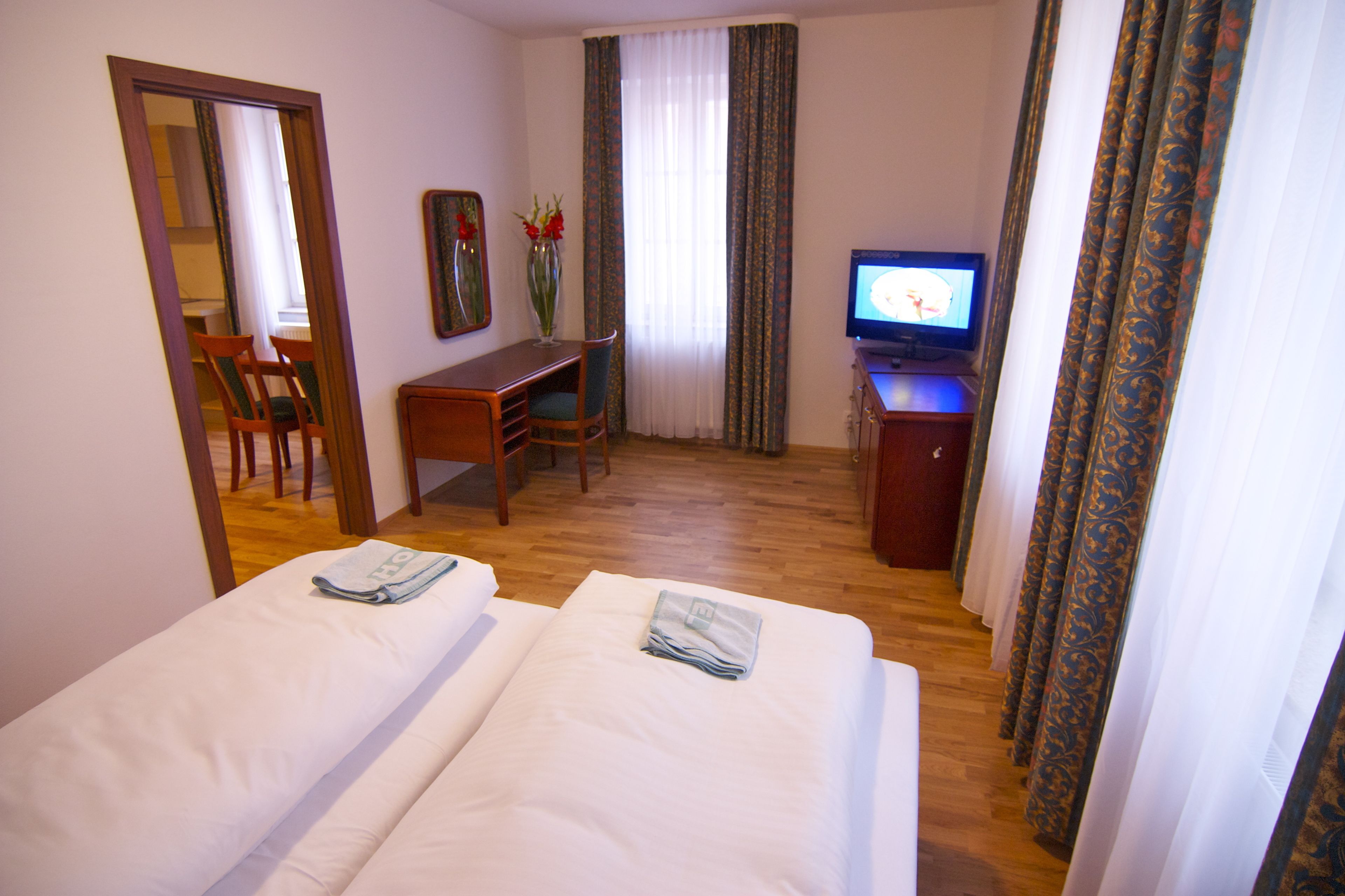 A hotel room with two beds, a desk, a chair, a television, and a mirror.