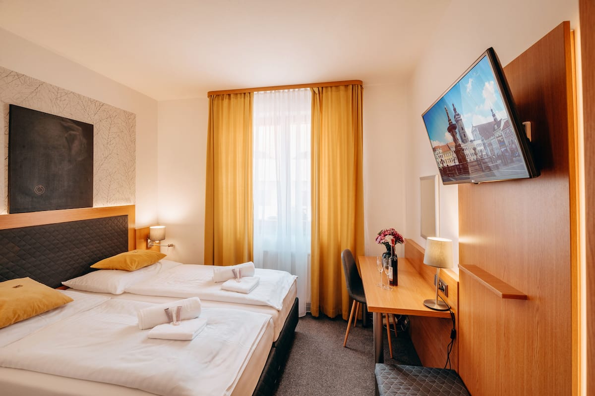 Habitación de hotel con dos camas, un escritorio con silla, televisión y ventana con cortinas.