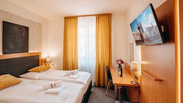 A hotel room with two beds, a desk with a chair, a TV, and a window with curtains.