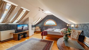 A spacious attic bedroom with a large bed, a television, a wooden desk, and a view through a skylight. - Hotel Klika (Ceske Budejovice)