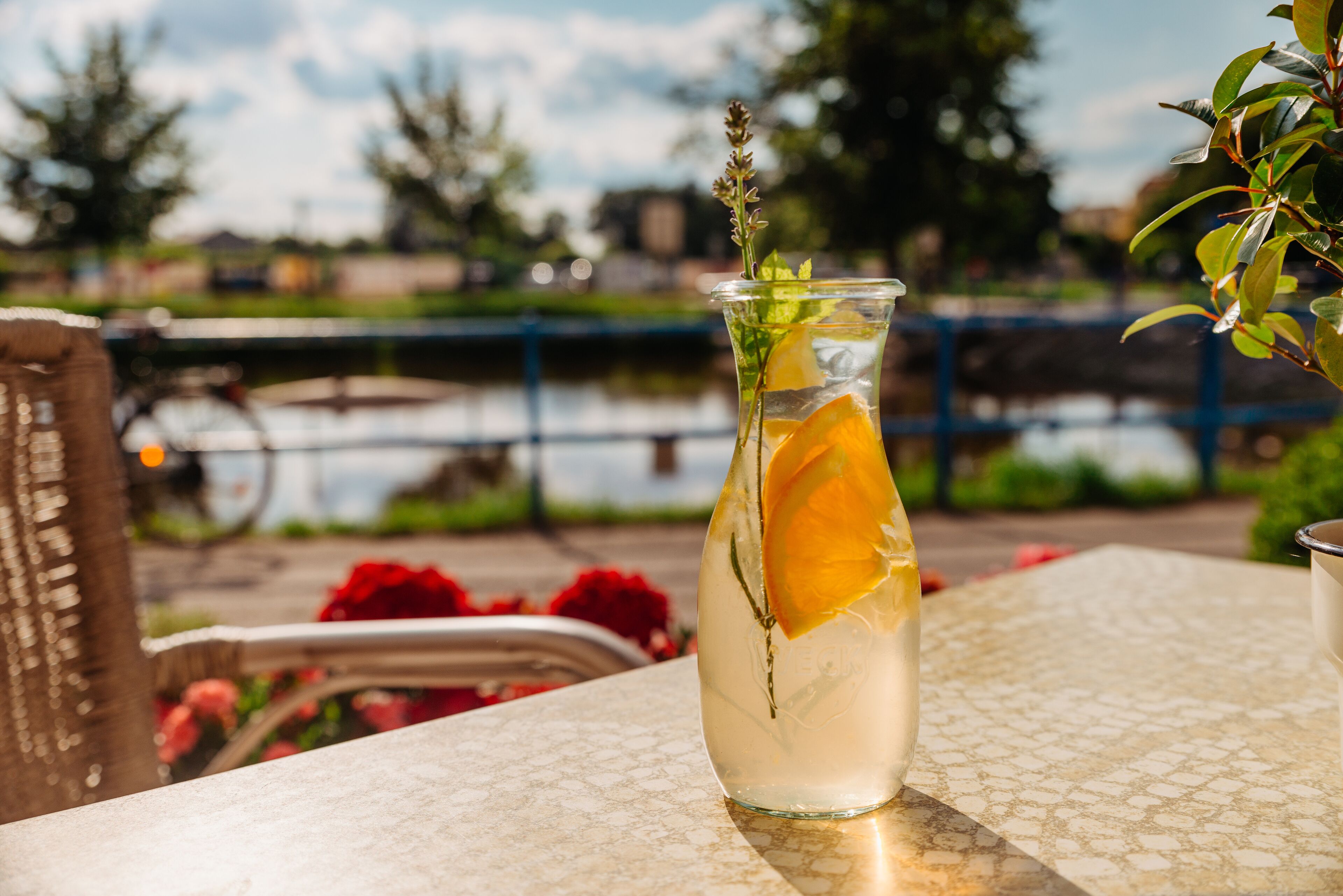 A clear glass bottle with a slice of orange and a sprig of herb on a table.