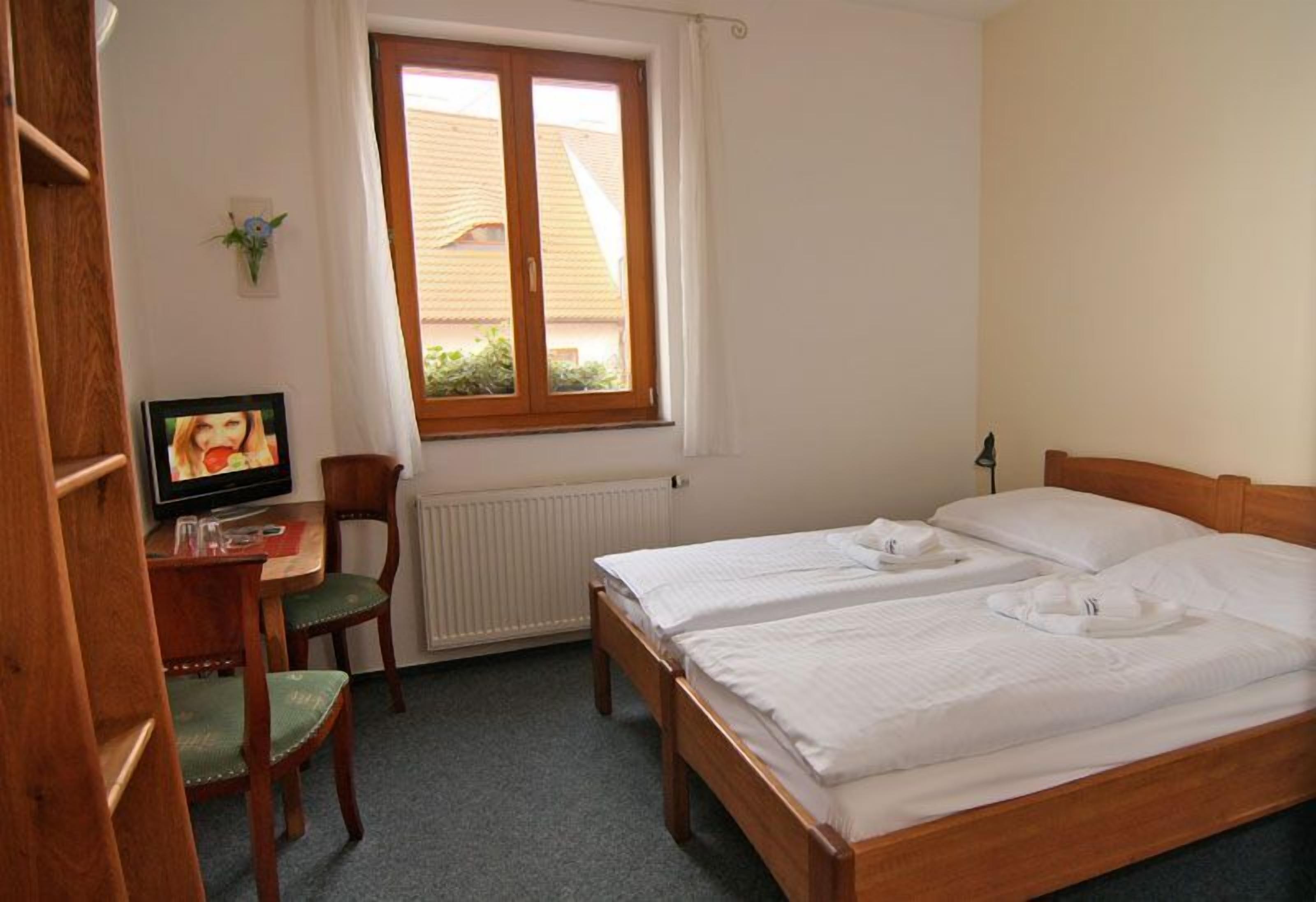Ett hotellrum med två sängar, ett skrivbord med en stol, en tv och ett fönster med utsikt över byggnader.