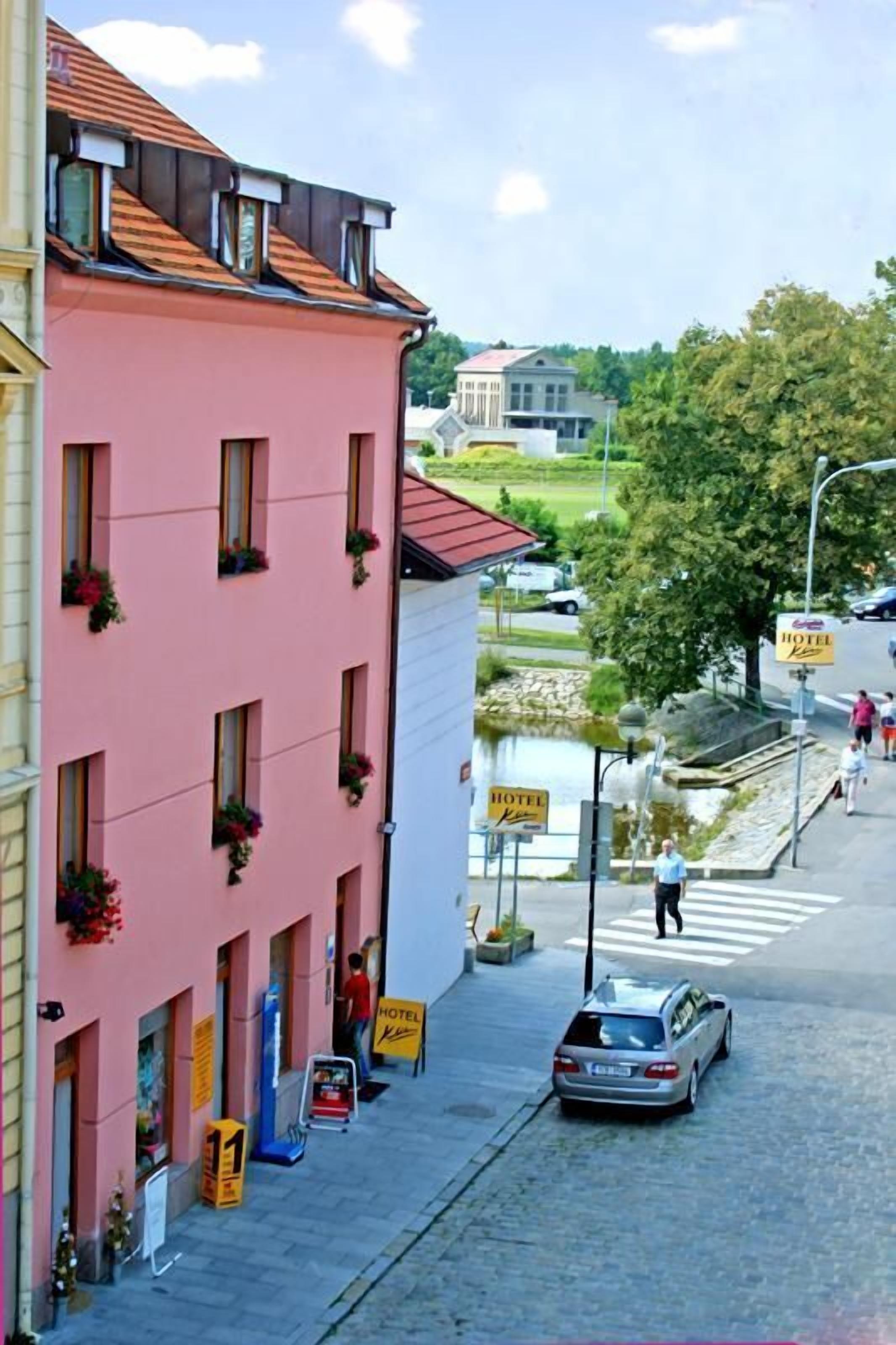 A pink building with multiple windows, a sign indicating a hotel, and a car parked on the street.