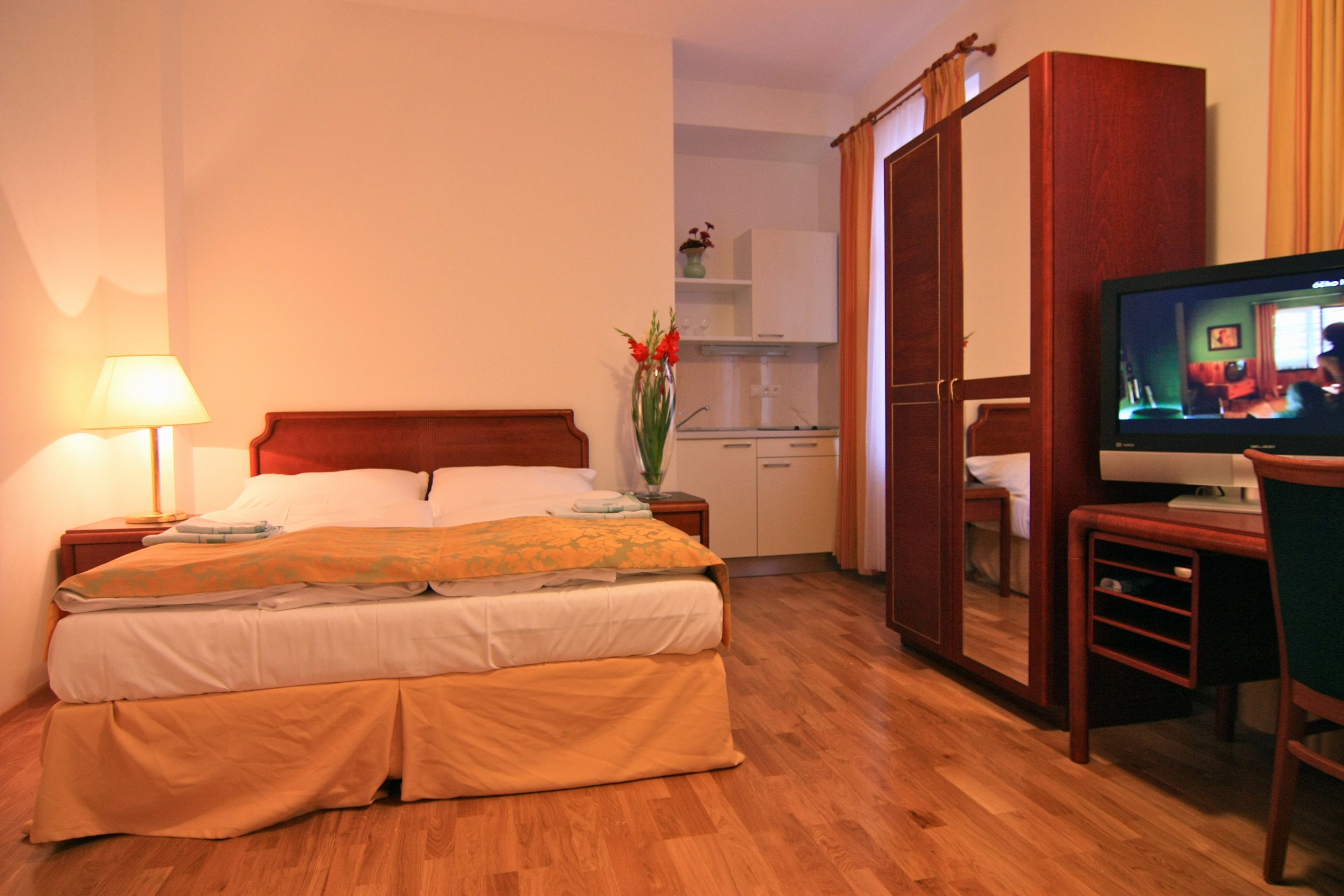 Une chambre d’hôtel comprenant un lit, une table de chevet, une lampe, une télévision et un petit coin cuisine.