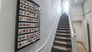 A hallway with a wall-mounted display of brochures and a carpeted staircase leading to an upper floor. - Tony's House Hotel (London)