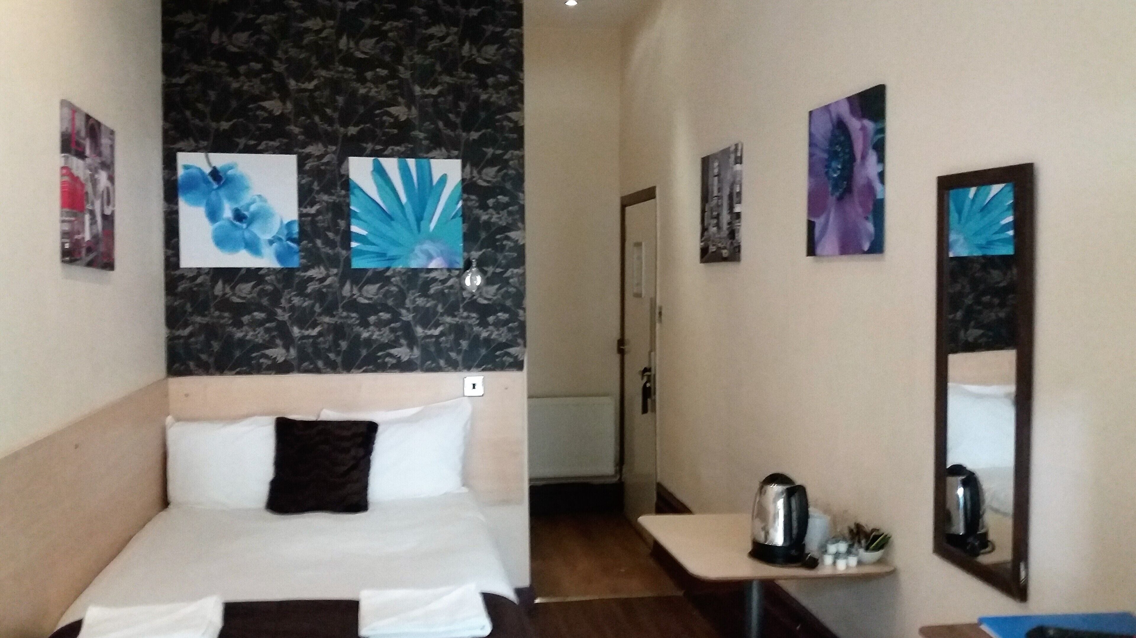 A hotel room with a bed, a small table with a kettle, and a mirror.
