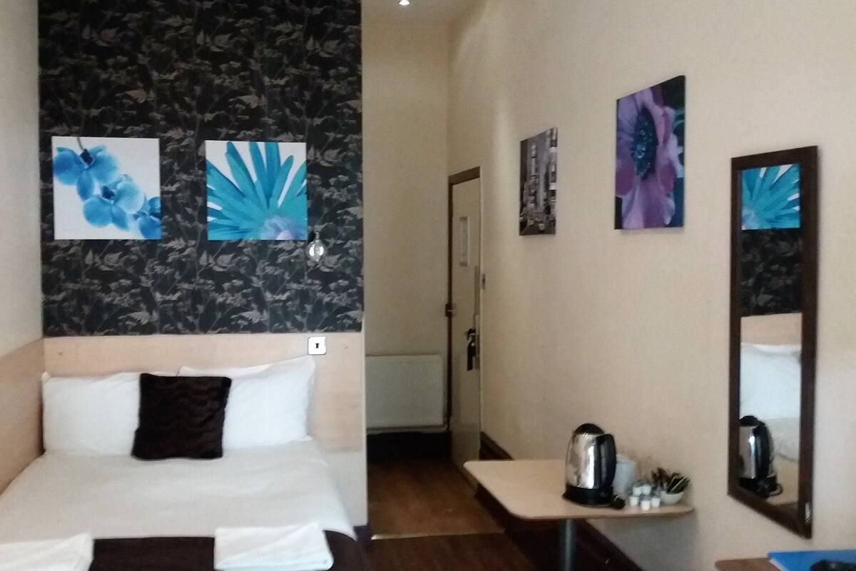 A hotel room with a bed, a small table with a kettle, and a mirror.