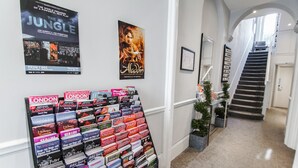 A hallway with a staircase, posters on the walls, and a display of travel brochures. - Tony's House Hotel (London)