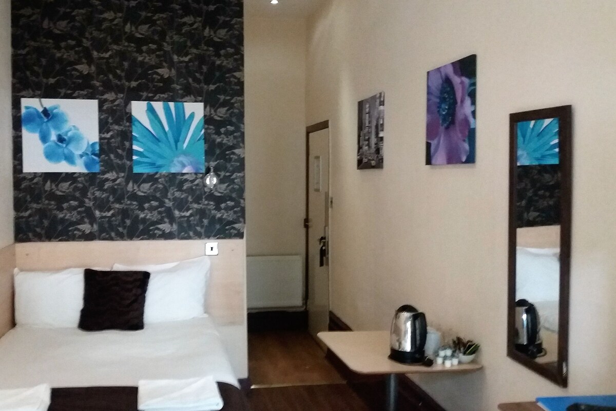 A hotel room with a bed, a small table with a kettle, and a mirror.