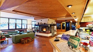 A cozy hotel lobby with a fireplace, green sofas, a wooden ceiling, and a sign for the Albergo Hotel. - Hotel Santa Caterina (Valfurva)