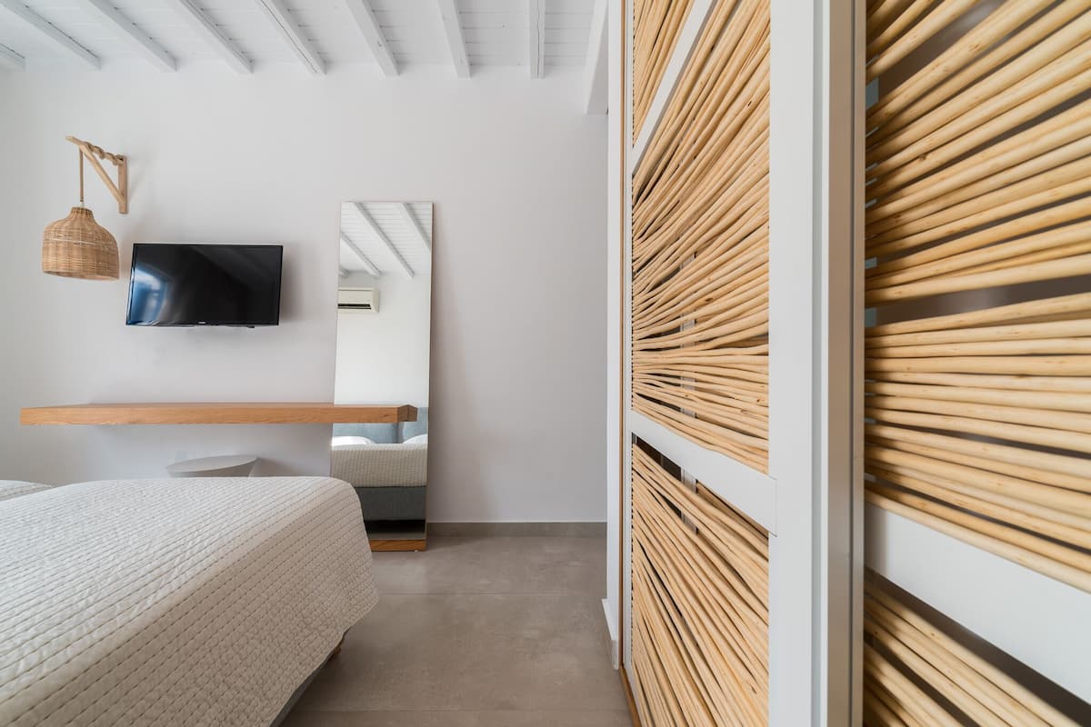 A modern bedroom with a bed, a mounted TV, a mirror, and a wooden slat wall.