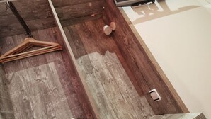 Una habitación con piso de madera, un televisor de pantalla plana montado en la pared, un mueble de madera con panel de control rojo, y un perchero.