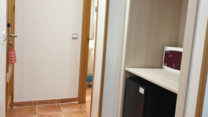 Un pasillo estrecho con una puerta que da a una habitación, un refrigerador pequeño y un armario con cerradura.