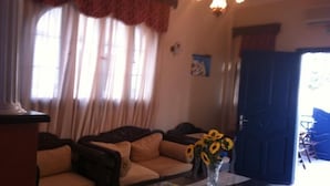 A living room with a sofa, a vase with sunflowers, and a door leading to another room. - Hotel Lignos (Santorini)