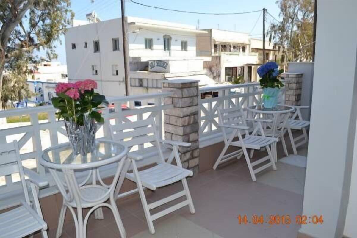 A balcony with white chairs and a table, a vase with flowers, and a view of buildings in the background.