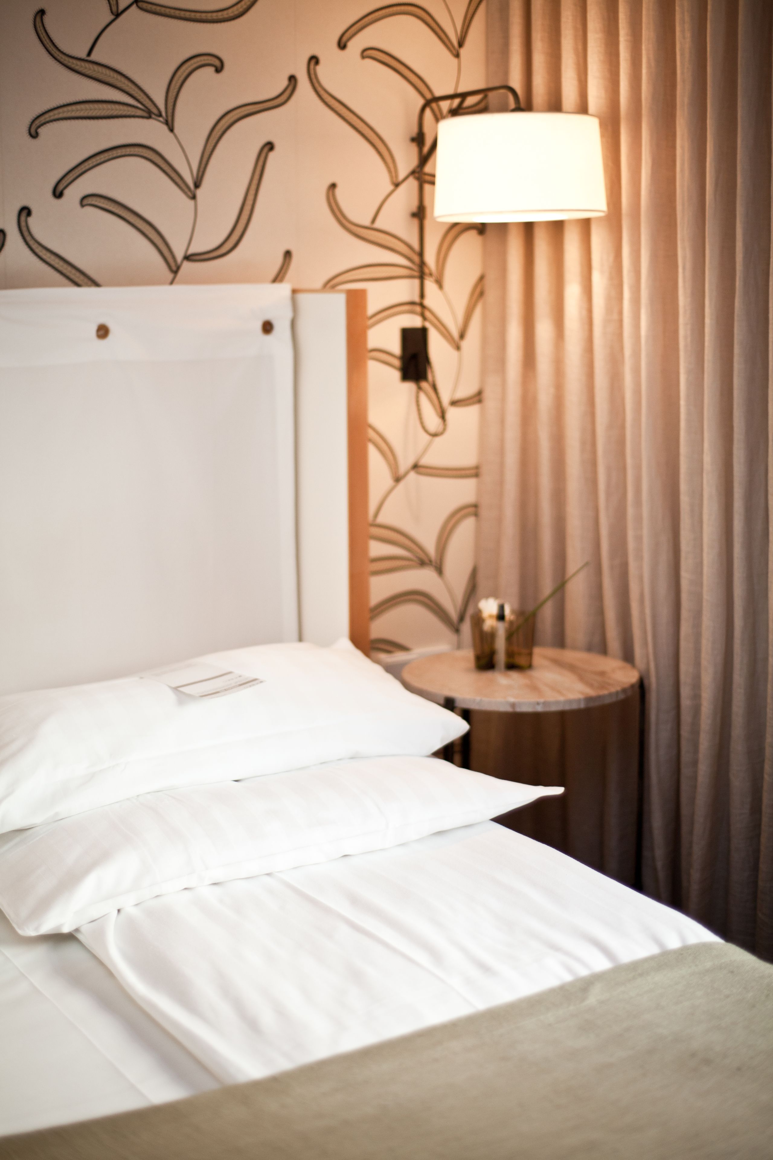 Une chambre d’hôtel avec un lit, une table de chevet, une lampe et des rideaux.