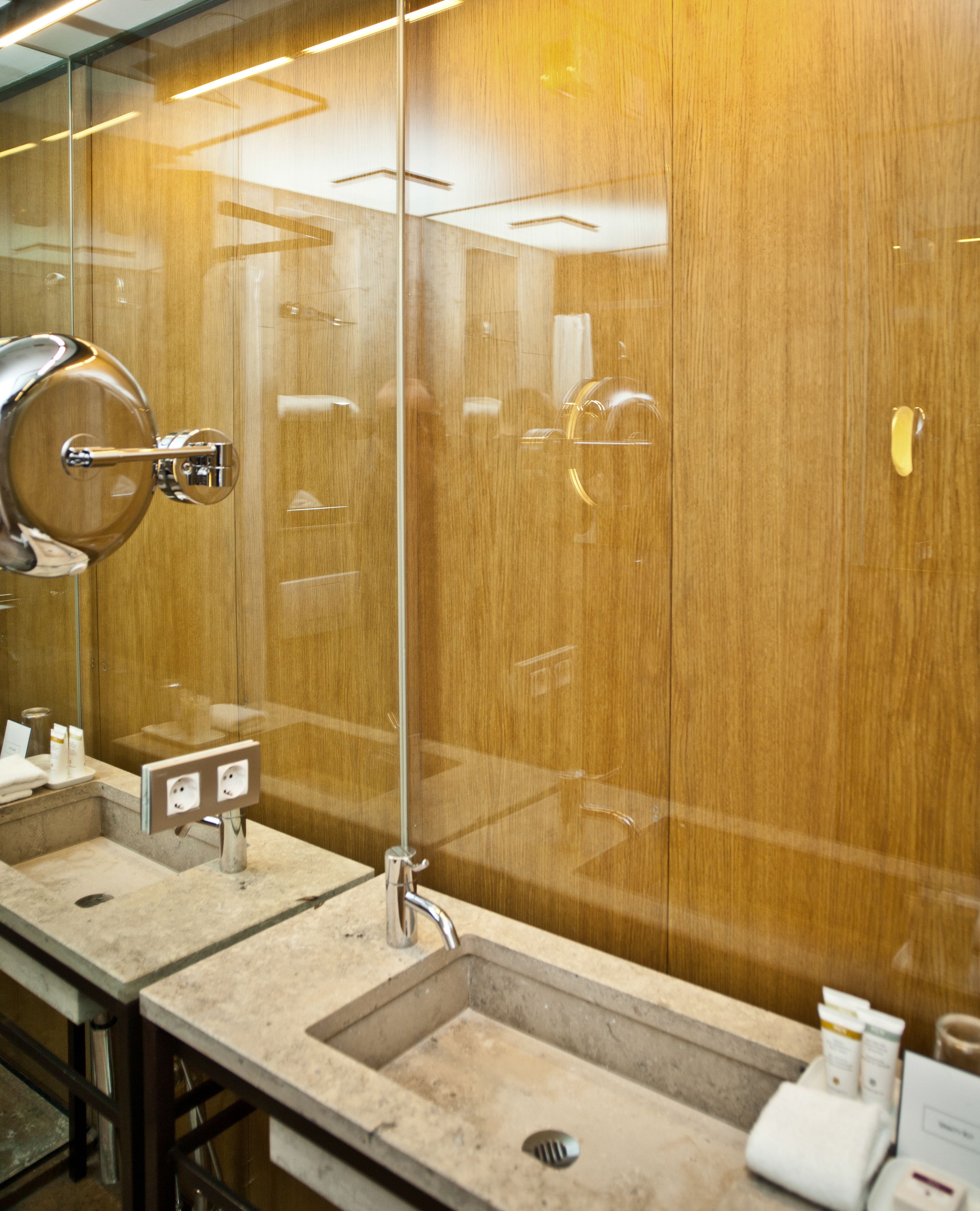 Un baño moderno con pared de madera, separador de vidrio y lavamanos con espejo.