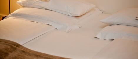 A neatly made bed with white linens and pillows, a bedside lamp, and a brown throw blanket.