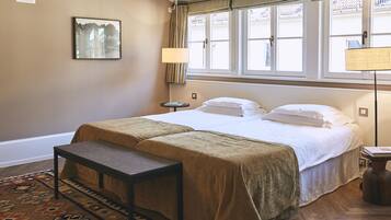 Una habitación de hotel con cama, mesitas de noche, un banco, un tapete y una ventana con cortinas.