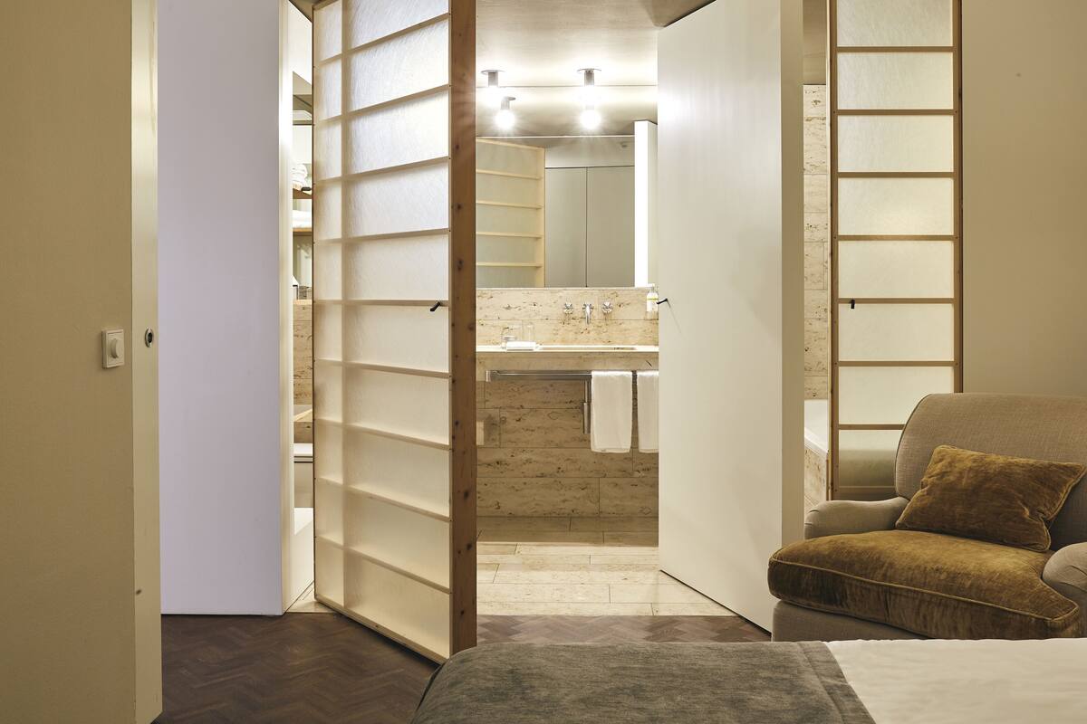 A room with a bed, a sofa, a bathroom with a mirror, and a wooden partition.