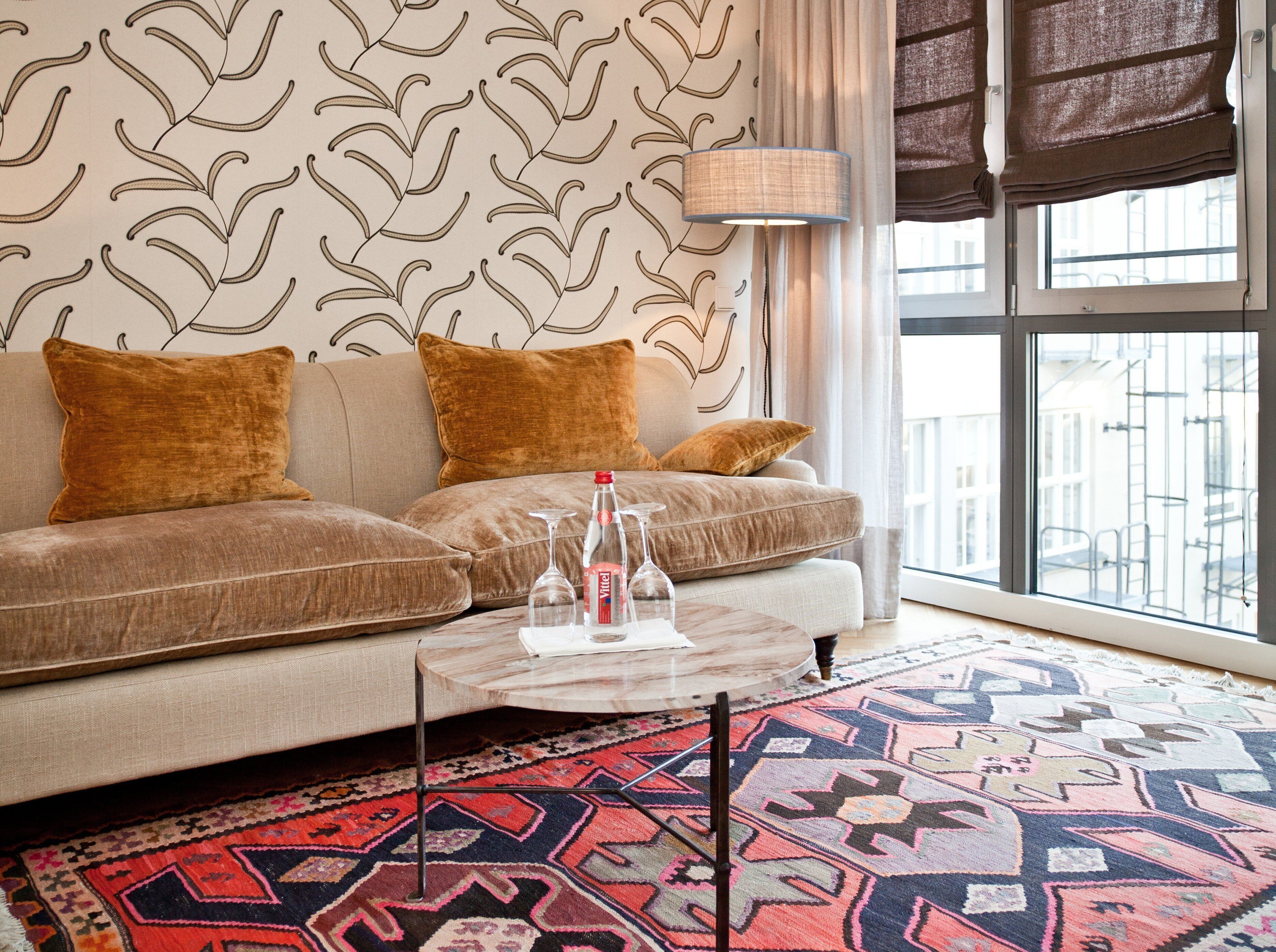 Un salon moderne avec un canapé beige, un mur à motifs et un tapis coloré.