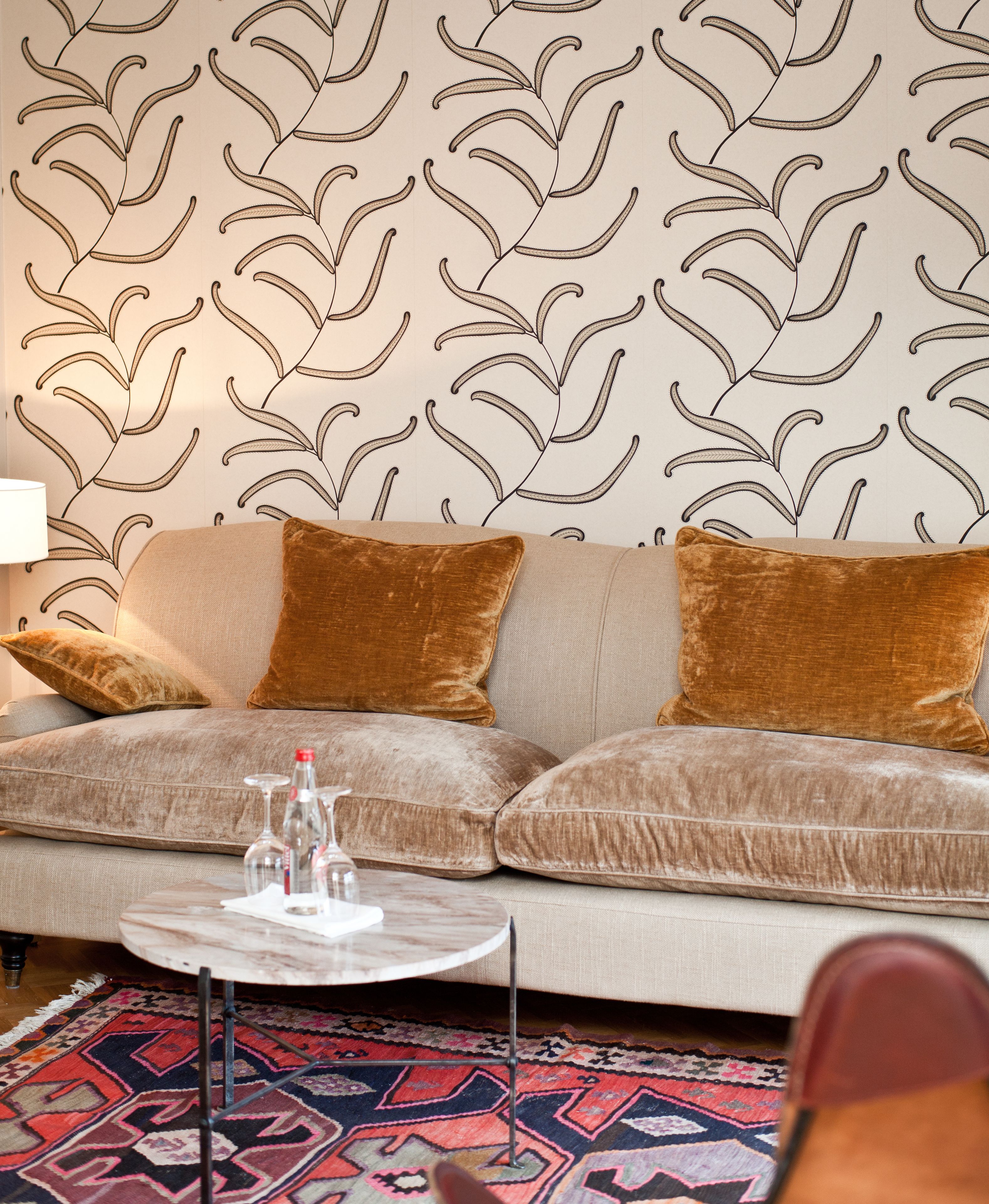 A living room with a sofa, two brown cushions, a glass coffee table, and a patterned rug.
