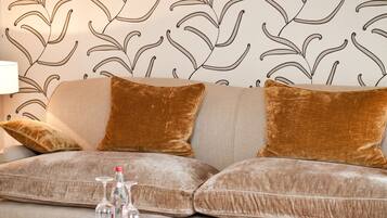 A living room with a sofa, two brown cushions, a glass coffee table, and a patterned rug.