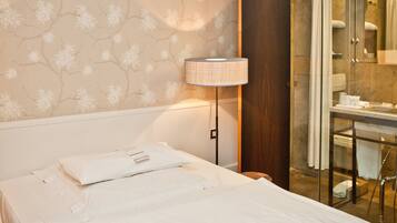 Quarto de hotel com cama, mesa de cabeceira, luminária e área de chuveiro.