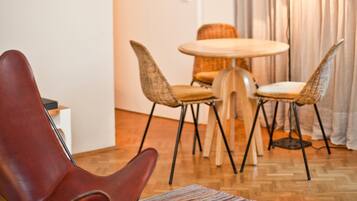 A modern living room with a red leather chair, a round wooden table, and two wicker chairs with cushions.