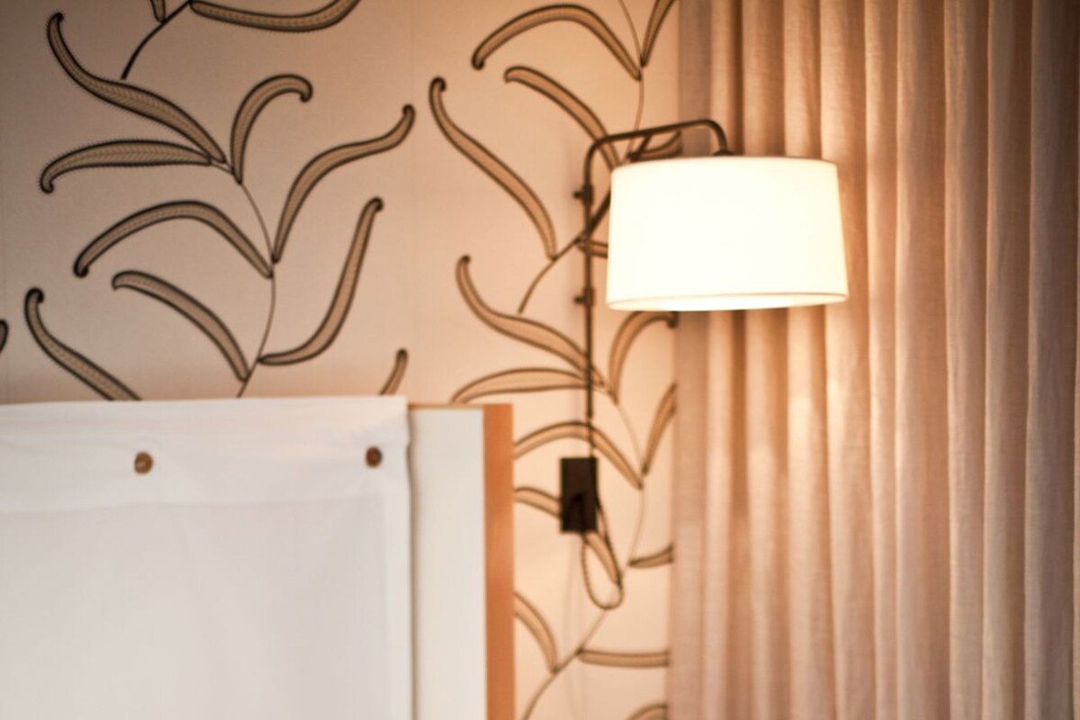 Une chambre d’hôtel avec un lit, une lampe de chevet, une petite table ronde et un rideau.