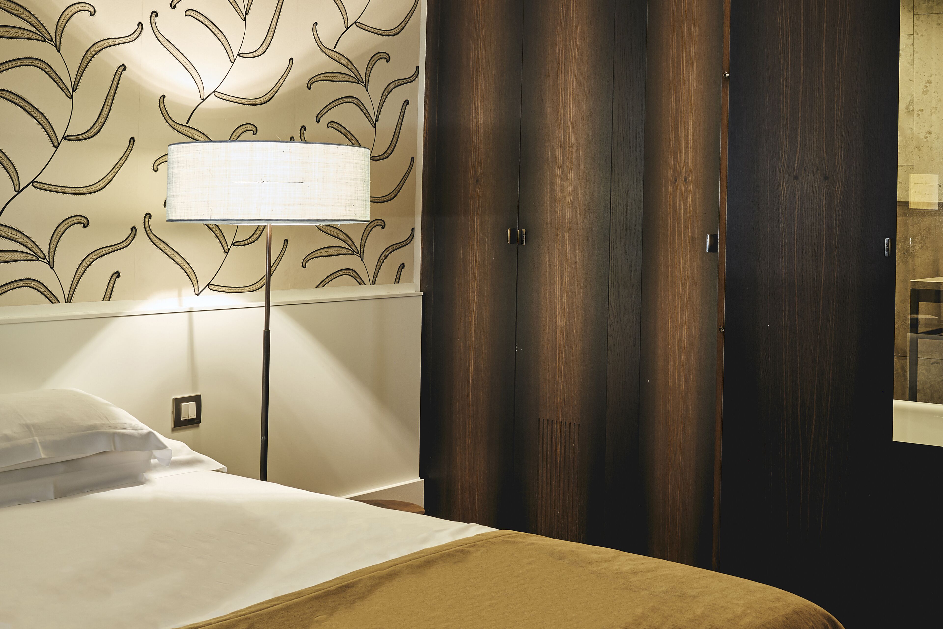 Ein Hotelzimmer mit einem Bett, einer Lampe, einem Kleiderschrank und einer Wand mit Blattmuster.