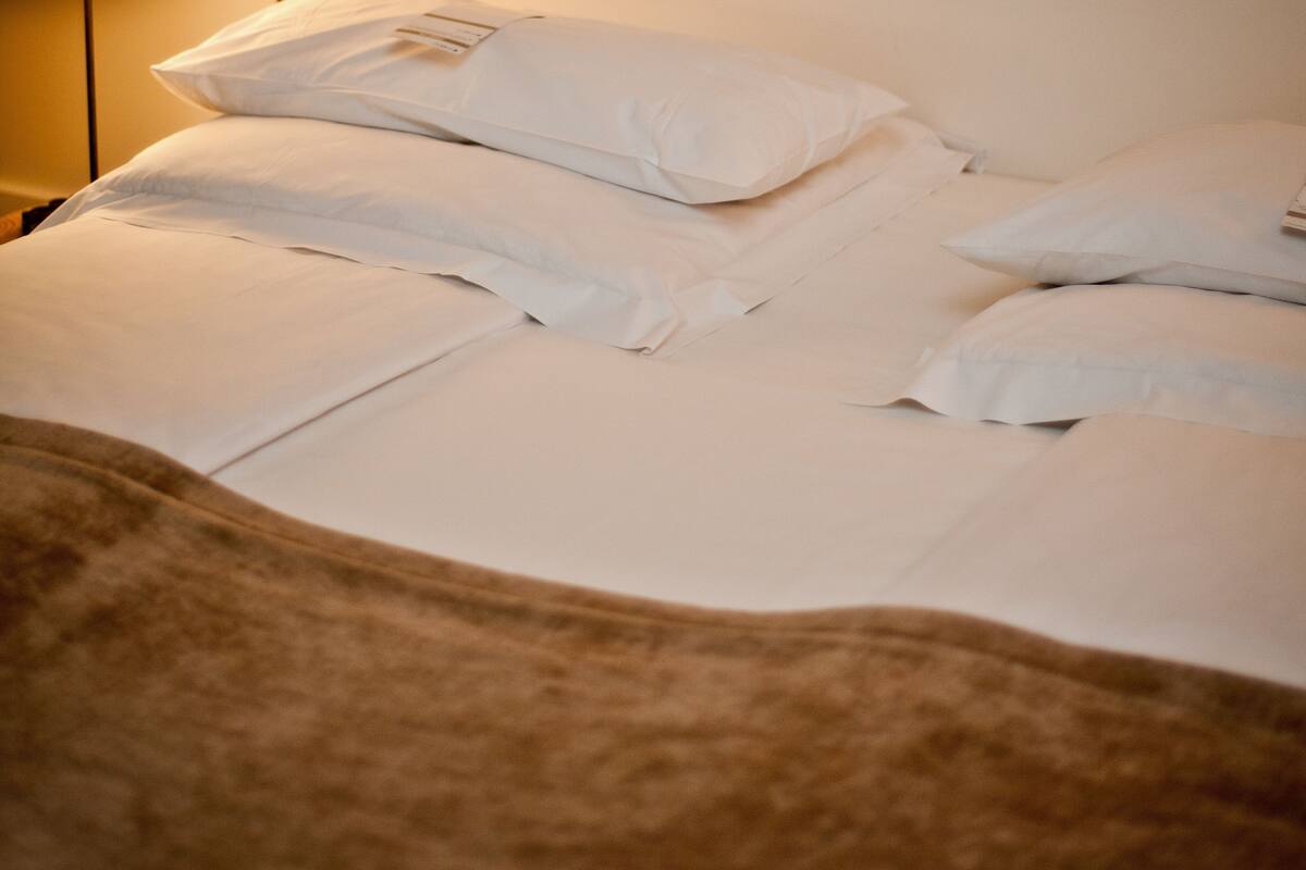 A neatly made bed with white linens and pillows, a bedside lamp, and a brown headboard.