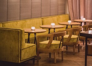 Un rincón acogedor con bancos tapizados de color amarillo y sillas de madera, cada uno con una pequeña mesa redonda.